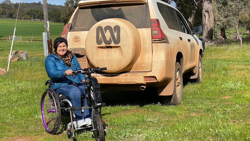 Woman in a wheelchair next to dusty four wheel drive with ABC logo on back.