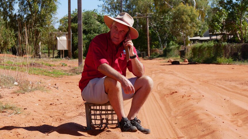Alan Gray sits on a milk crate while talking on a phone.