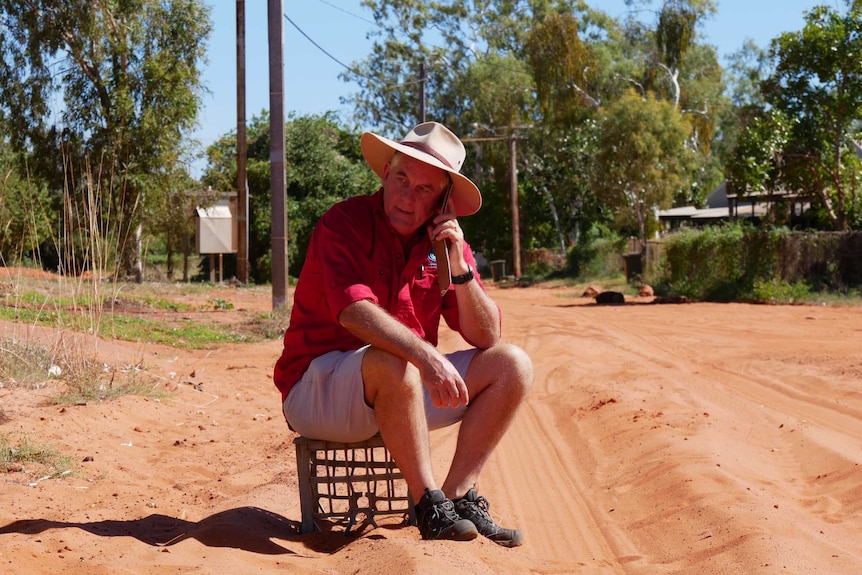 Alan Gray sits on a milk crate while talking on a phone.