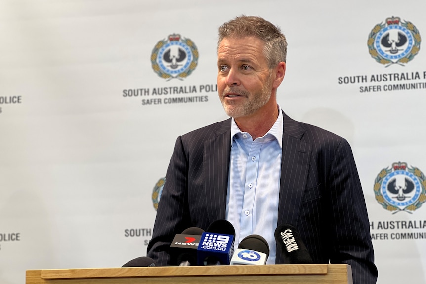 A man wearing a suit jacket and white shirt in front of a police logo background