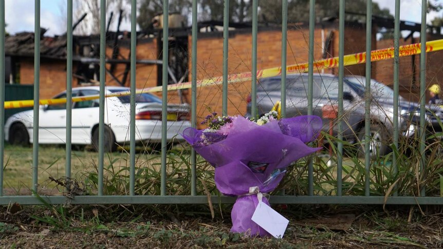 Flowers are placed in front of a fence at the burnt down house.