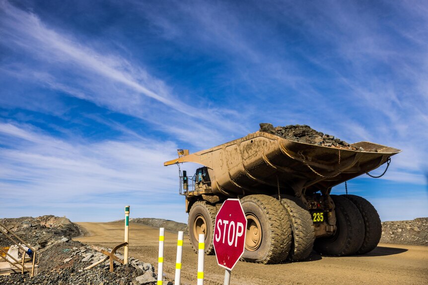 A mining truck loaded with rock in the back driving past a stop sign.  
