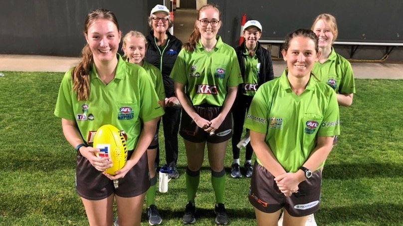Seven girls stand in a group in green umpire shirts.