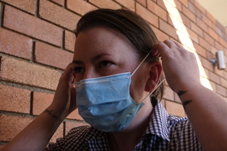 A woman puts a face mask on.
