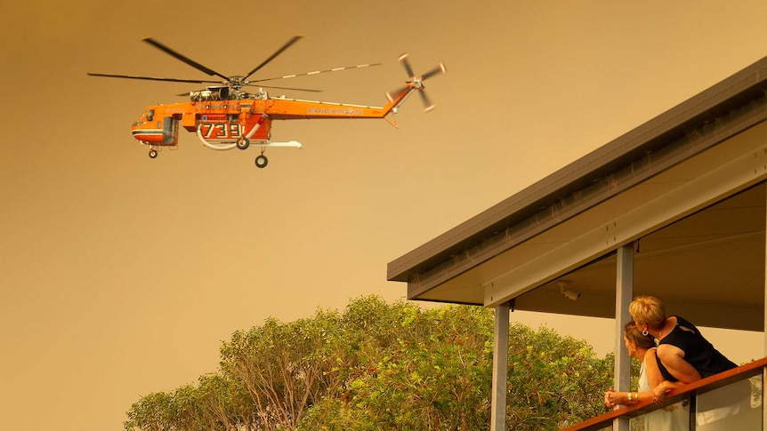 Residents watch on from a balcony as a helicopter flies over during fire fighting efforts