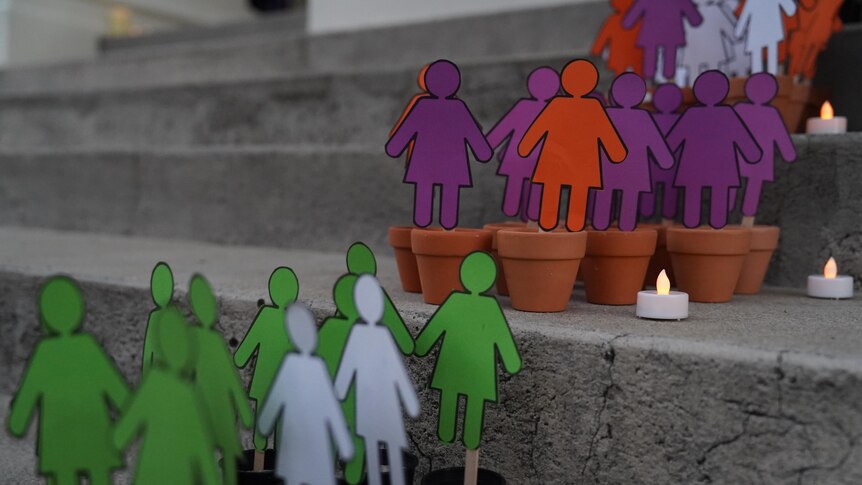 Colourful cut outs representing women in small terracotta pots beside tea light candles.