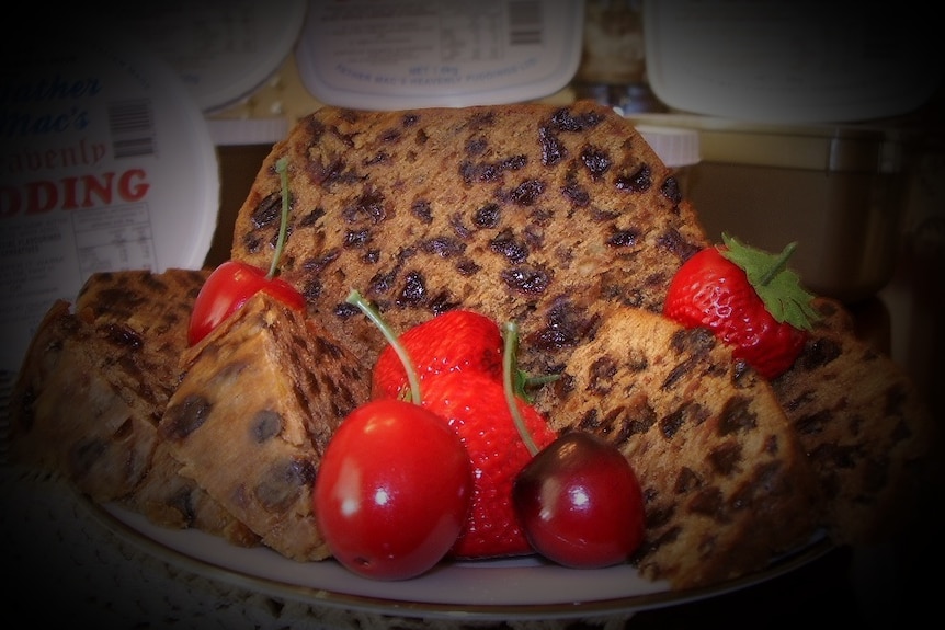 A close up of a pudding on a plate with red cherries and strawberries