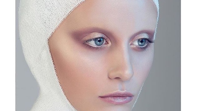 A model with a white bandage wrapped around her head and shimmering pink make-up.