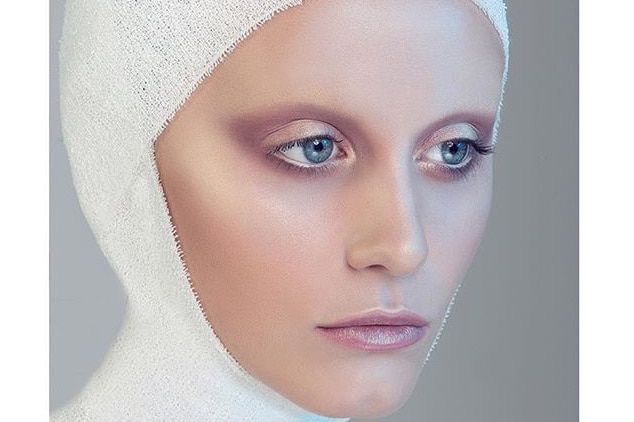 A model with a white bandage wrapped around her head and shimmering pink make-up.