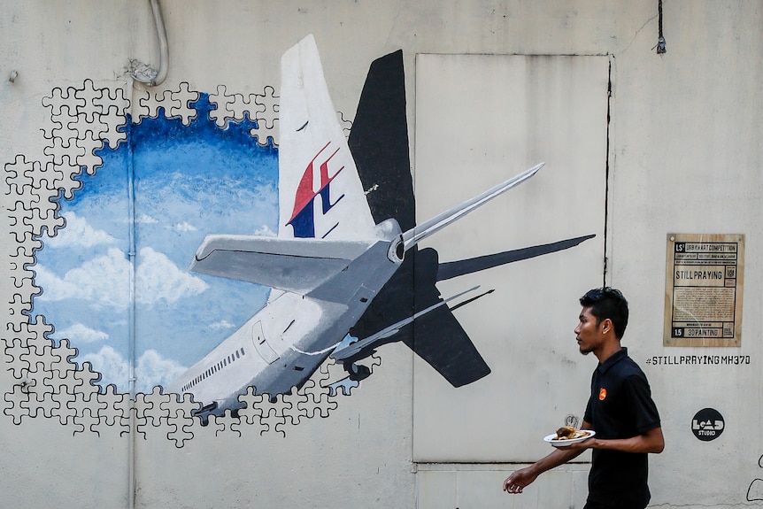A man walks past a mural of the MH370 plane flying through a hole made of puzzle pieces. 