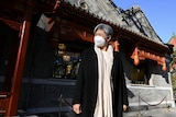 戴着口罩、外套和围巾的黄英贤站在一座华丽的中式建筑前。