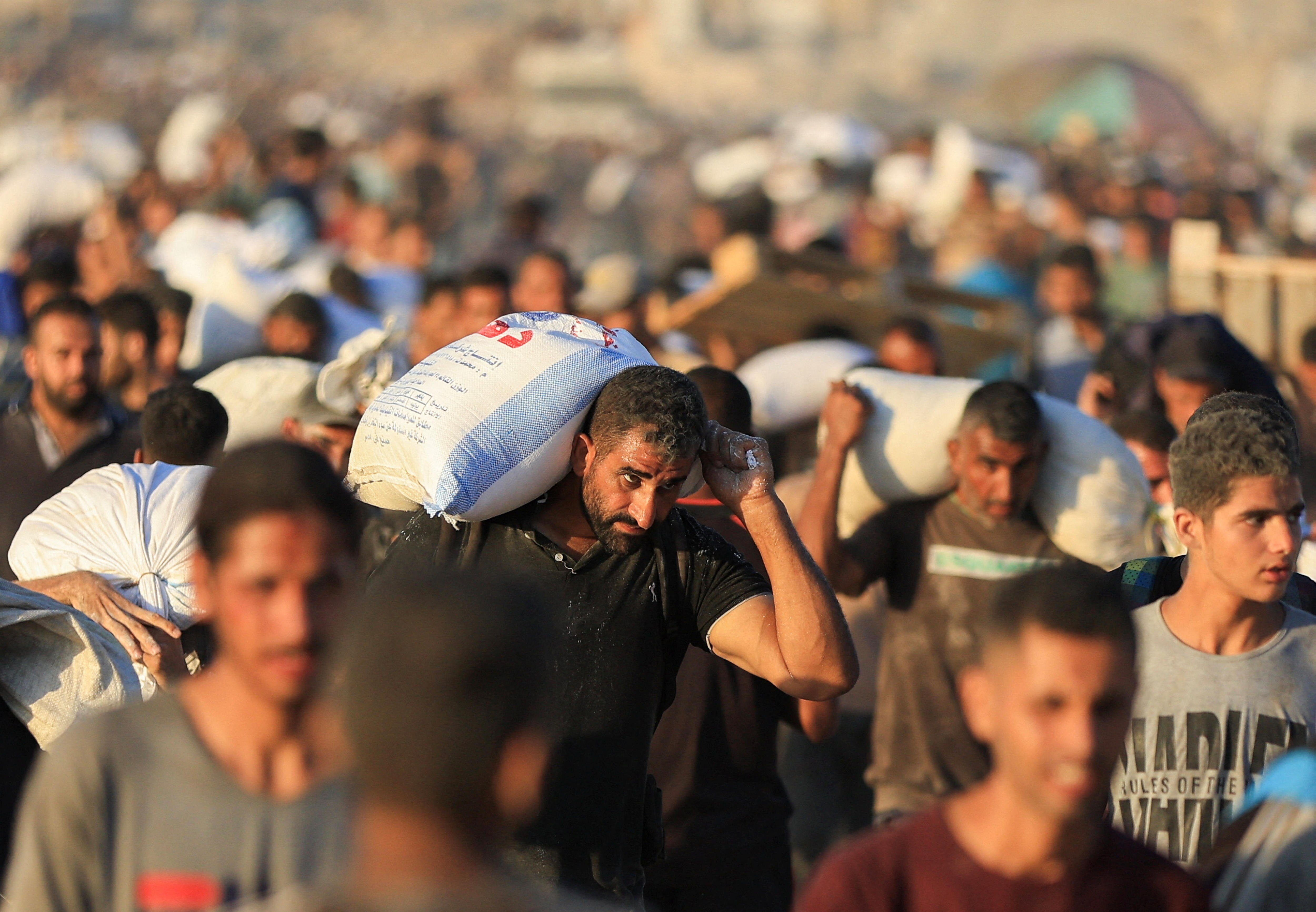 A crowd of people carry white flour bags 