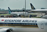 Several airplane fuselages bearing blue and gold Singapore Airlines branding are visible on the runway of a crowded airport.