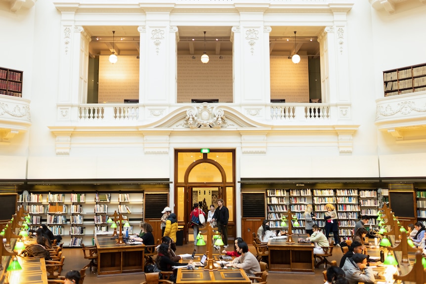 A Victorian reading space in a library with high ceilings, book shelves and people sitting at tables