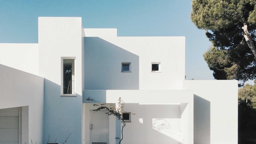 A white, flat-roofed concrete house with white tiled path to depict where the all-white house trend came from.