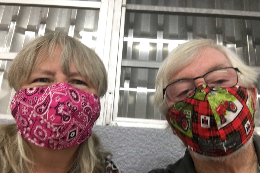 Barbara, left, wears a pink face mask and appears to smile underneath it next to John, right, in a green and red mask.