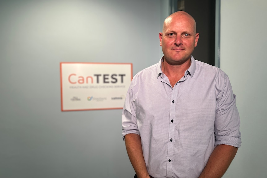A bald man wearing a pink shirt in front of a sign that says CanTest