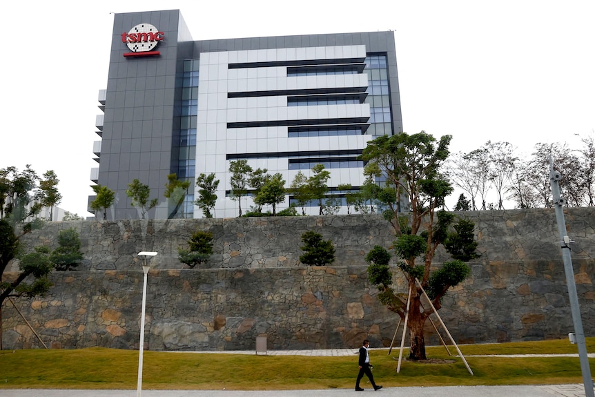 A person walks pass a building with a red and white TSMC sign.
