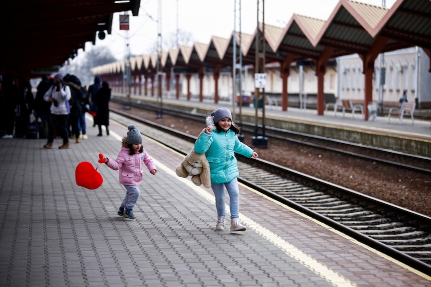Two young children play on a platform at an empty train station.