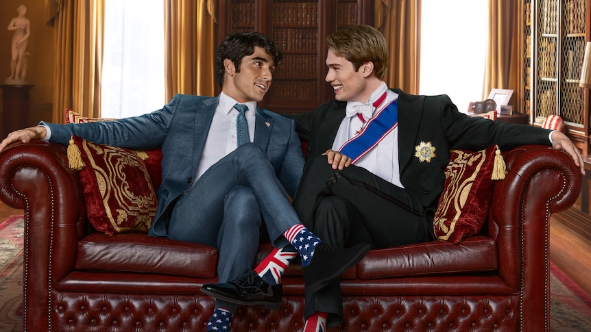 Characters Alex and Henry sit on a couch in red white and royal blue, wearing socks bearing the flags of their countries.