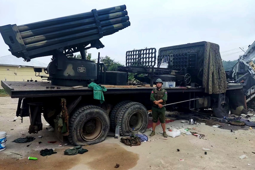 A soldier stands in front of a truck mounted rocket launcher.