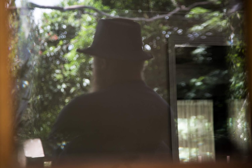 Ben stands with his back reflected in a window.