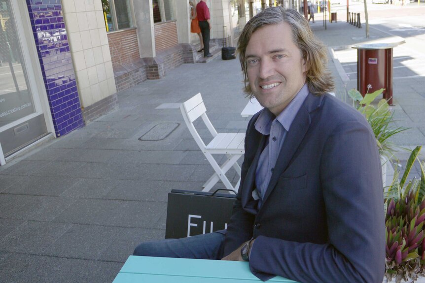 Michael Tucak wearing a suit and sitting on a bench on a city street.