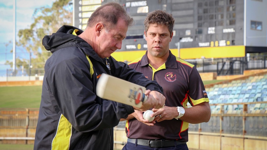 Geoff Marsh wields a cricket bat while Dane Ugle watches on with a ball in his hand.