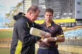 Geoff Marsh wields a cricket bat while Dane Ugle watches on with a ball in his hand.