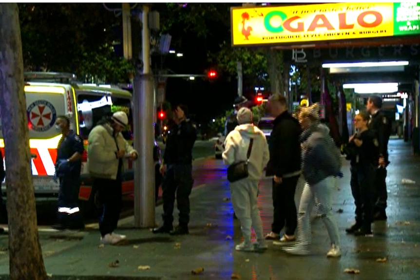 People standing on a street, with an ambulance in the background