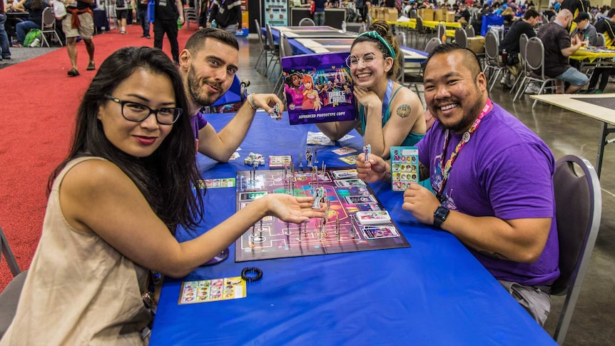 A group of people sitting around a table playing a board game in a convention centre