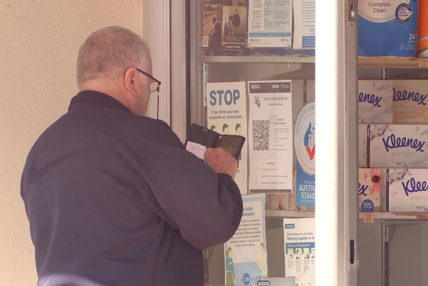 A man holds a cellphone to a QR code on a pharmacy window