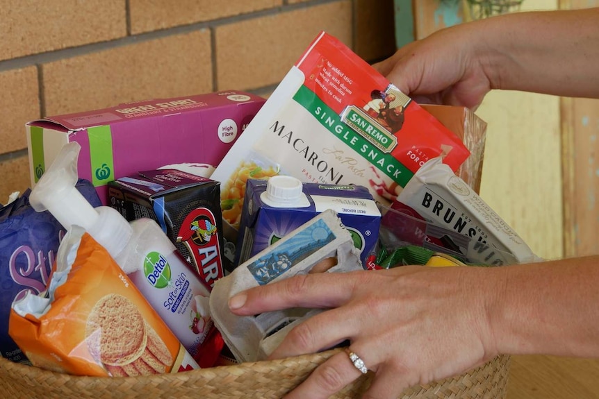 A hamper of food sits on a table while a woman's hand picks out some pasta.