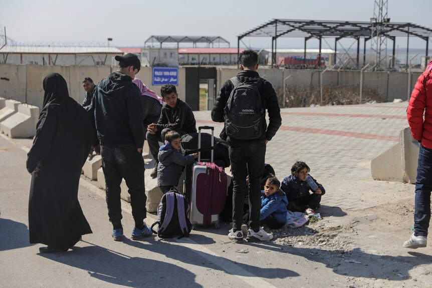 Family with suitcases stand together at border crossing.