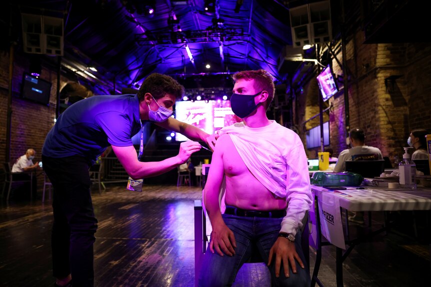 A man who has lifted up his shirt receives a COVID-19 jab in a London nightclub.