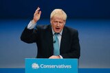 Britain's Prime Minister Boris Johnson holds his hand to the arm as he speaks from a podium.