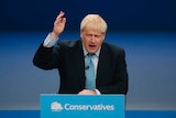 Britain's Prime Minister Boris Johnson holds his hand to the arm as he speaks from a podium.