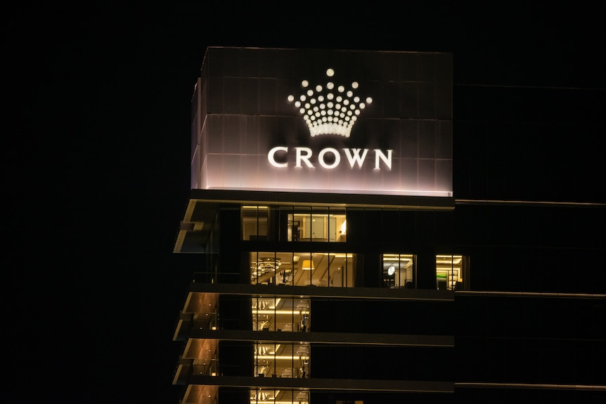 Bangunan tinggi dalam gelap dengan lampu menyala dengan tanda yang menyala dengan kata Mahkota di bawah simbol mahkota.