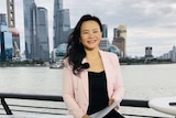 Journalist Cheng Lei is seen smiling while seated with the Shanghai waterfront in the background.