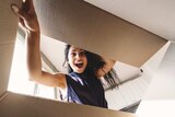 A woman looking surprised and happy looks into an open cardboard box