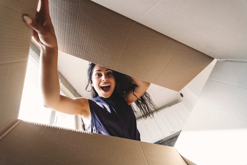 A woman looking surprised and happy looks into an open cardboard box