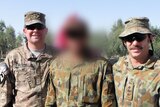 Three men in army fatigues standing together, the middle has his face blurred completely