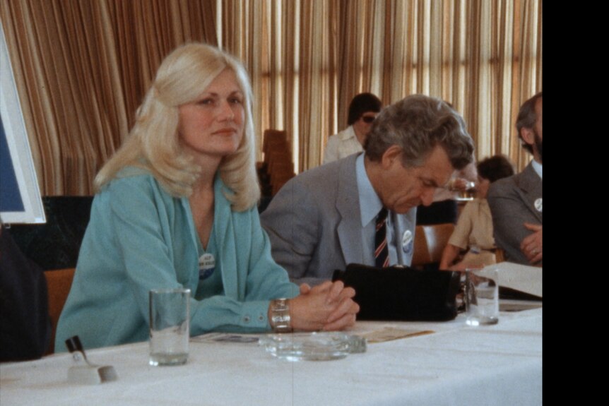 A blonde woman in a blue suit sits with Bob Hawke.