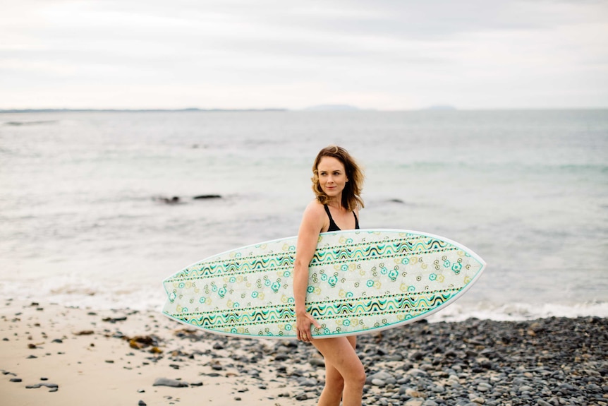 Jada McNeil surf board designer standing on beach with green board.