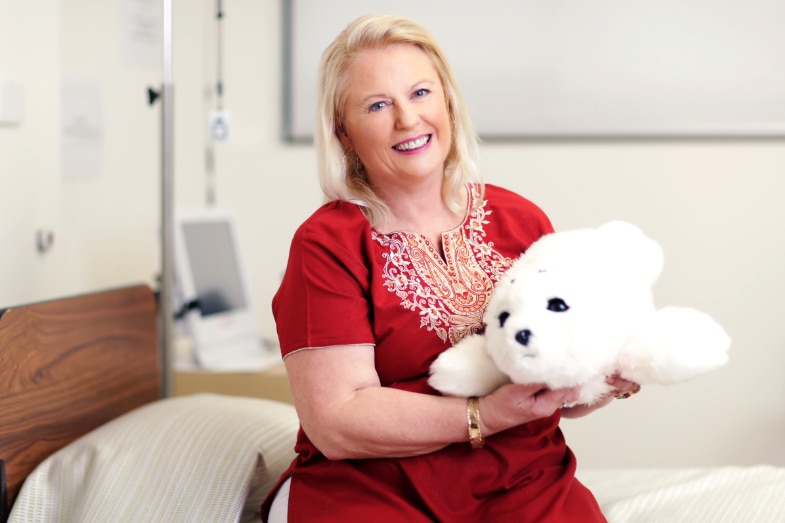 A woman in a red shirt and blond hair smiles at the camera holding a plush seal toy