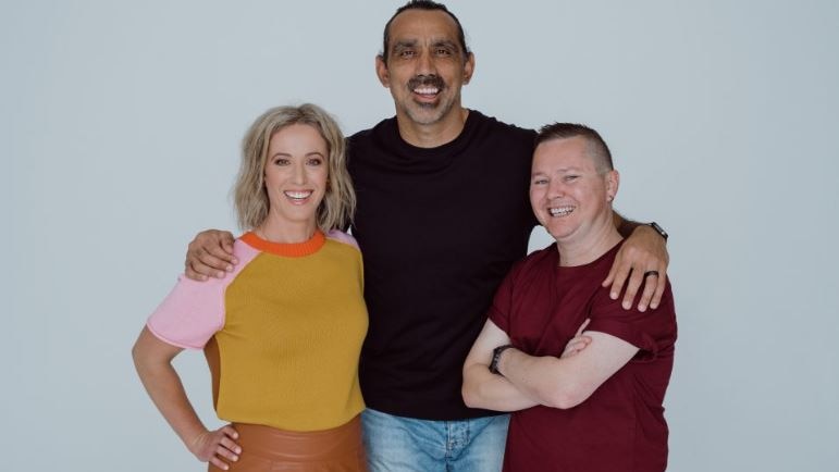 aboriginal man in black t-shirt with arms around the shoulders of a blonde woman in a yellow t-shirt and man in maroon t-shirt