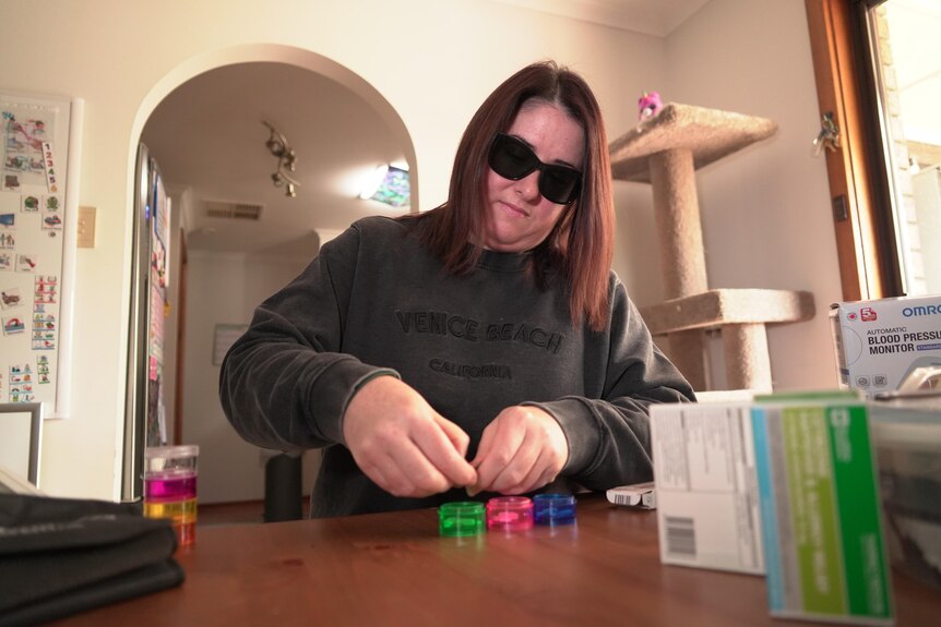 A woman wearing sunglasses and a black jumper takes medication from small boxes