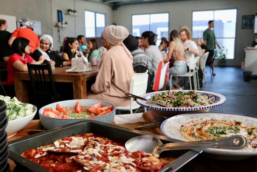 A large group of people eating food with dishes in the foreground of the shot.