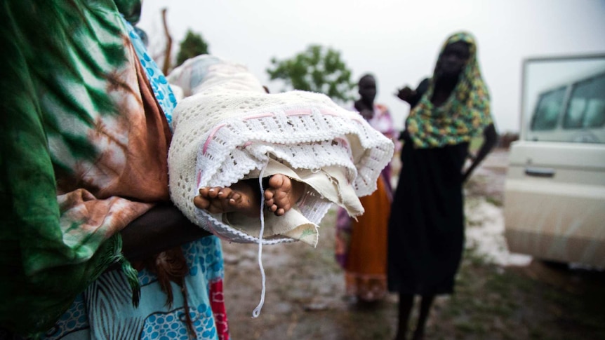 An aunt holds the body of baby Nyanene, whose tiny feet stick out of a blanket.