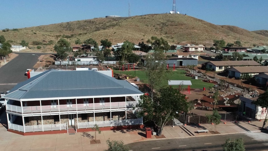 Aerial view of two-storey building with white verandahs in a town with a hill in the background.